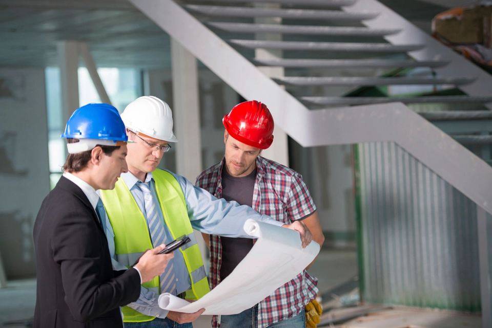 Three people in hard hats reviewing building plans