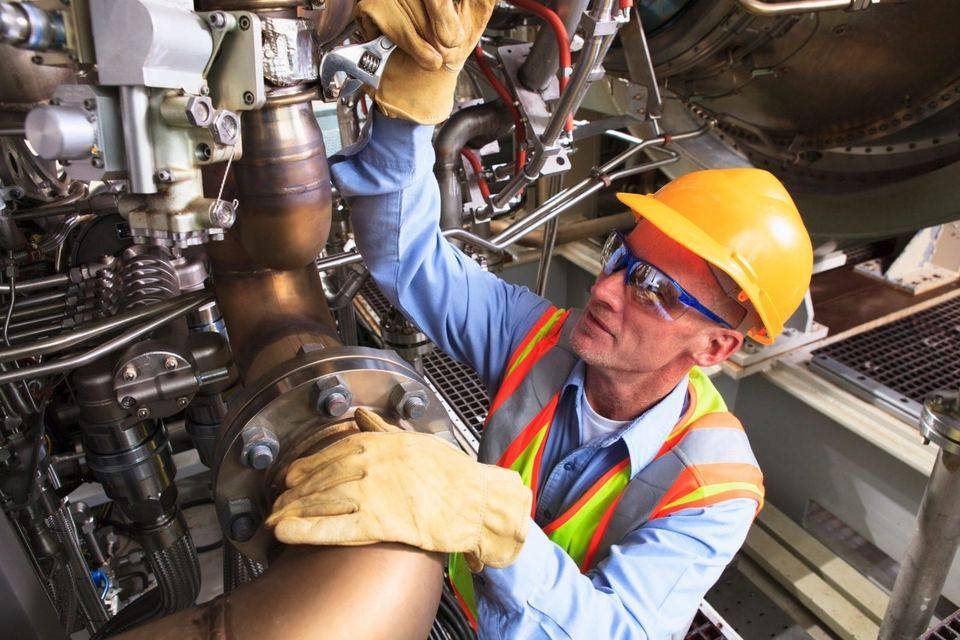 Technician in a hard hat and safety vest working on machinery