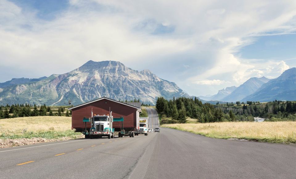 A house being hauled on a truck along a highway, mountains behind